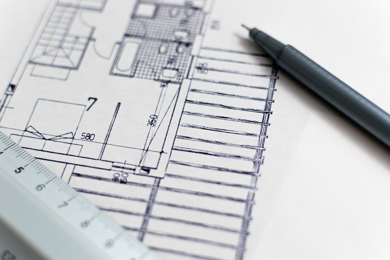 Plano arquitectónico sobre una superficie plana. El plano está compuesto por líneas finas y
símbolos que representan las diferentes partes de un edificio, como paredes, puertas,
ventanas y habitaciones. Se pueden apreciar números y medidas en el plano, lo que indica
las dimensiones de las diferentes áreas. Junto al plano, hay una regla y un bolígrafo
instrumentos utilizados para tomar medidas o realizar anotaciones