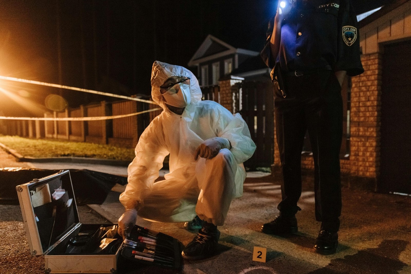 Fotografía de Investigador forense recogiendo pruebas. Fotografía de Investigador forense
con traje protector blanco y herramientas en escena del crimen nocturna. Forense
investigando con la policía. Investigador haciendo análisis forense en la escena del crimen.
Escena de crimen nocturna. Forense en procedimiento policial.