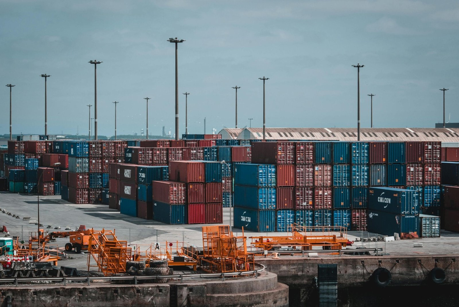 Un puerto de carga con numerosos contenedores apilados de diversos colores y grúas visibles en
el fondo. El cielo está despejado. Esta imagen podría ser relevante para temas relacionados con la
logística, la industria del transporte marítimo, negocios de importación/exportación o el comercio
global.