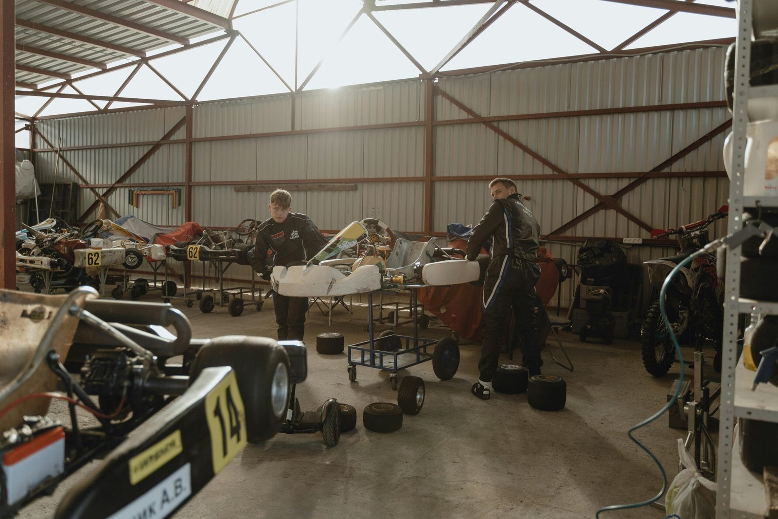 La imagen muestra un ambiente relacionado con la Ingeniería en Sistemas Automotrices,
donde dos personas, posiblemente estudiantes o profesionales, trabajan en lo que parece
ser un taller de karts de carreras o automóviles pequeños. Ambos están vestidos con trajes
de carreras, lo que refuerza la temática automotriz.